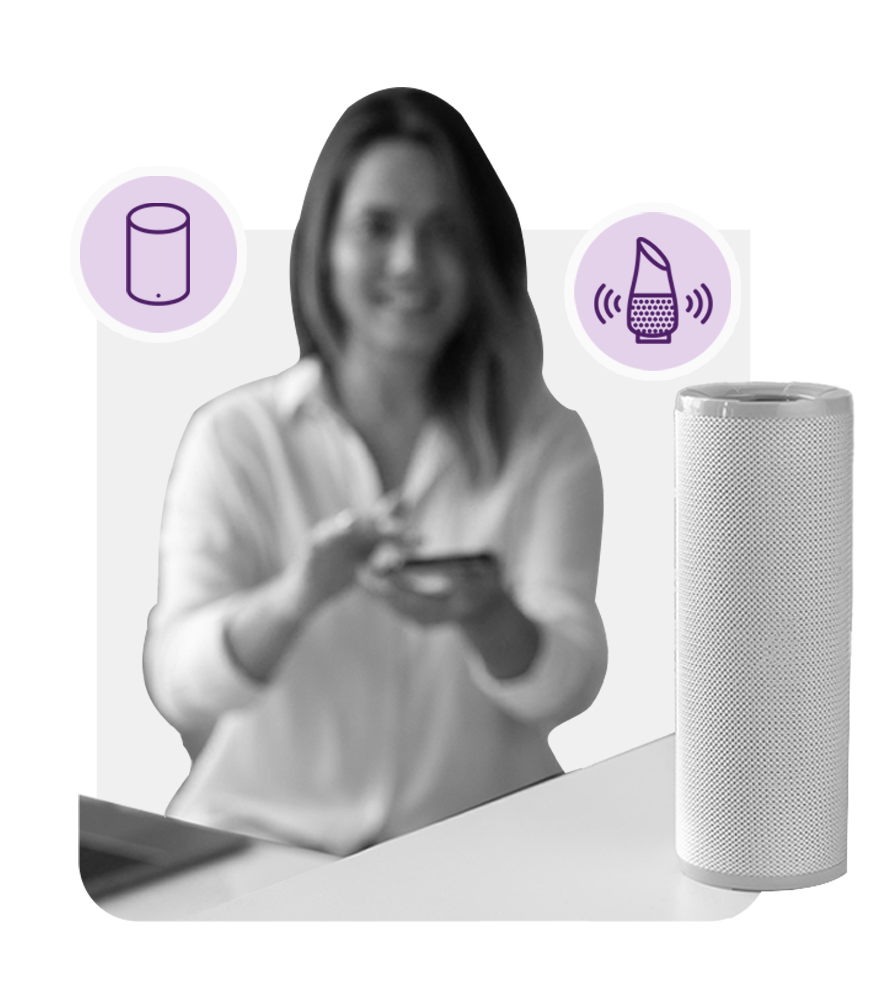 A woman holding a smart phone next to a smart speaker.